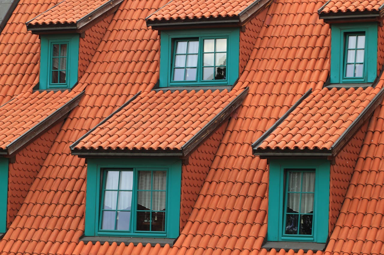 portfolio-06 Close-up of an orange tiled roof with green framed dormer windows, creating a colorful architectural contrast.